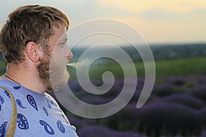 young man smokes on a blurred background of a lavender field. Lifestyle