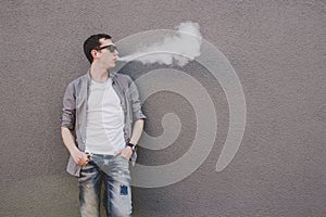 Young man smoking, vaping electronic cigarette or vape. Gray background