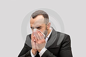 Young man sneez into white tissue. He keeps eyes closed. Young man is sick. Isolated on white background.