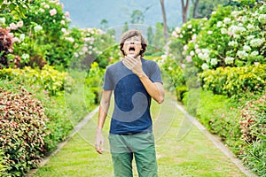 Young man sneeze in the park against the background of a flowering tree. Allergy to pollen concept photo