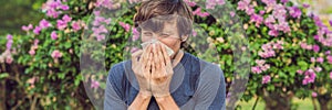 Young man sneezes because of an allergy to pollen BANNER long format