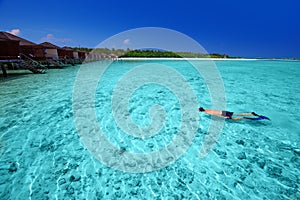 Young man snorkeling in tropical island with overwater bungalows