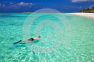 Young man snorkling in tropical lagoon with over water bungalows, Maldives