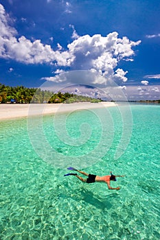 Young man snorkling in tropical lagoon with over water bungalows, Maldives photo