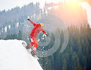 Young man snowboarder jumping from the top of the snowy hill with snowboard in the evening