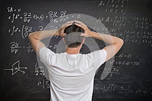 Young man is solving mathematical problem on blackboard and is confused