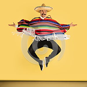 Young man in sombrero and bright poncho isolated over yellow background