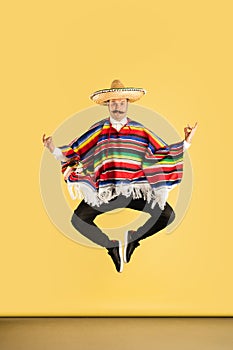 Young man in sombrero and bright poncho isolated over yellow background