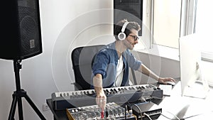 Young man in sound recording studio. Guy sit in front keyboard and using music mixing console. Listening to music