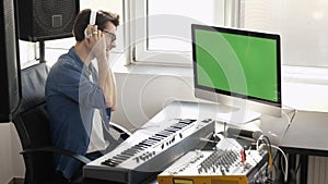 Young man in sound recording studio. Sit alone and using music mixing console with computer. Digital green screen