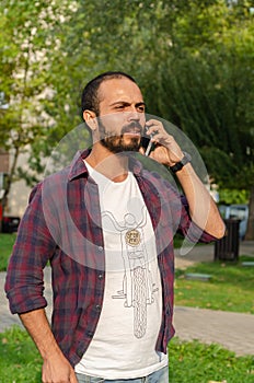 The young man is speaking at his cell phone at the park