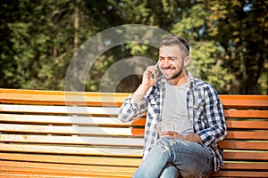 Young man speaking over mobile phone on the bench outdoors