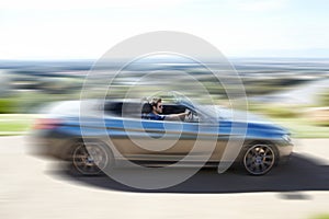 Hes a speed freak. A young man speeding on the open road in his silver convertable. photo