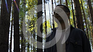 Young man spending time alone in summer forest. Stock footage. Walking along pine trees on a sunny day.