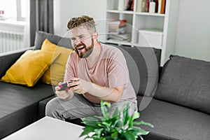 Young man spending time at home, sitting on a couch in apartment and playing arcade car video games on console. Male
