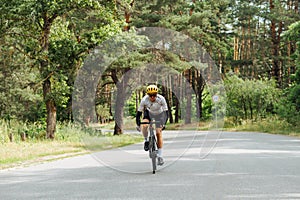 Young man in sports equipment trains in the woods outside the city and rides on an asphalt road