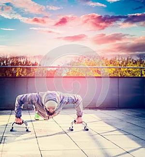 Young man in a sports suit and beard doing push-ups on the terrace the house overlooking the sunset sky and city