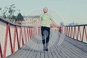 A young man in sportswear is jumping on jump ropes on bridge