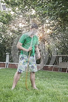 Young man spraying himself with a garden hose in the face, outdoors in the garden