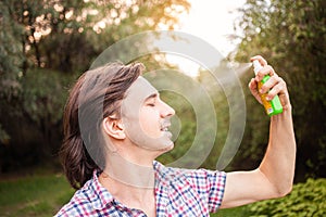 Young man spraying mosquito insect repellent in the forrest, protection. A man sprays mosquito spray on his face