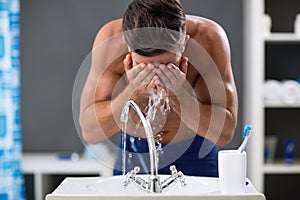 Young man spraying water on his face after shaving