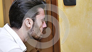 Young man spying through the keyhole of a door