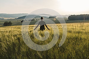 Young man stand in rural czech landscape with wheat field, hill and trees at sunset