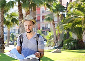 Young man standing alone outside with backpack and map