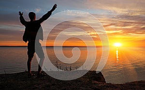 Young man standing with arms outstretched at sunset