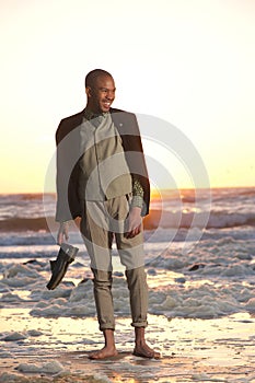 Young man standing on the beach with shoes in hand
