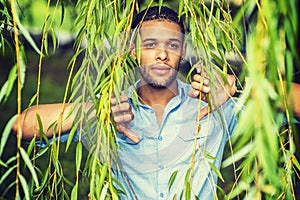 Young man standing behind long green leaves, looking forward