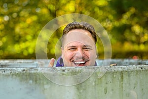 Young man standing behind a round concrete wall, laughing heartily