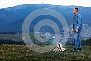 Young man standing by a burning fire under the evening sky in the mountains. Active lifestyle concept