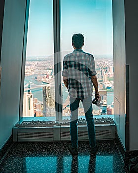 Young man standing with a camera and looking out of a window at One World Observatory