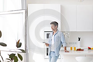 Young man standing on domestic kitchen holds digital tablet searching recipes for cook vegetable salad healthy food