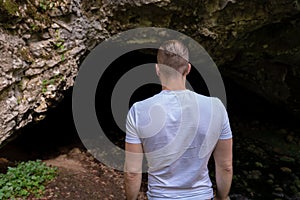 Young man standing in front of a cave entrance and looking into the darkness