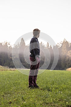 Young man standing in green meadow looking into distance