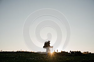 Young man standing on the hill field with hiking backpack and sticks