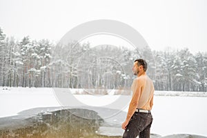 Young man standing by ice hole and ready to swim in the winter water