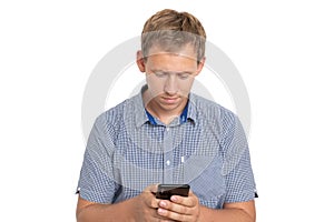 Young man standing looking at his phone screen, chatting with friend, wearing blue shirt isolated on white background