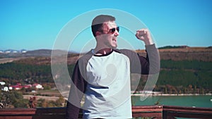A young man is standing, looking from the observation deck and bouncing up, raising his hands and showing super signs