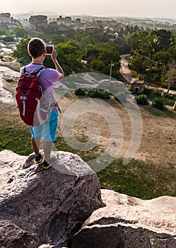 Young man standing on a mountain and making photo of the valley