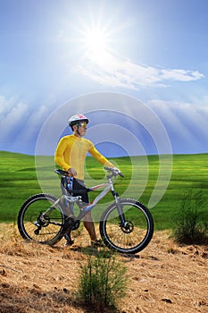 young man standing beside moutain bike ,mtb on hill with sun shining on blue sky use for sport leisure and out door activities ex