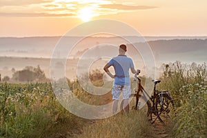 Young man standing near bicycle in morning sunrise with wonderf