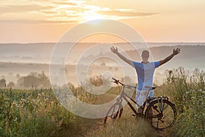 Young man standing near bicycle in morning sunrise with wonderf