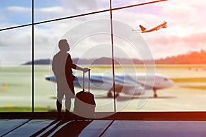 Young man is standing near window at the airport and watching pl