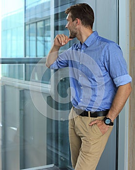 Young man standing near window in his office while thinking about his goals.