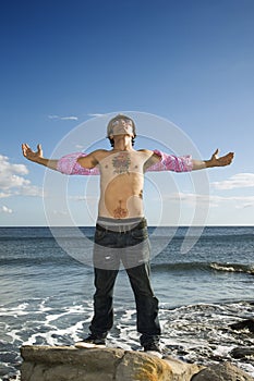 Young Man Standing on Ocean Rock with Arms Outstre