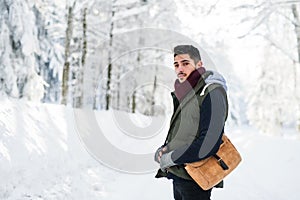 Young man standing outdoors in snow in winter forest, looking at camera.