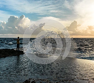 Young man standing with raised hands in front of raging sea